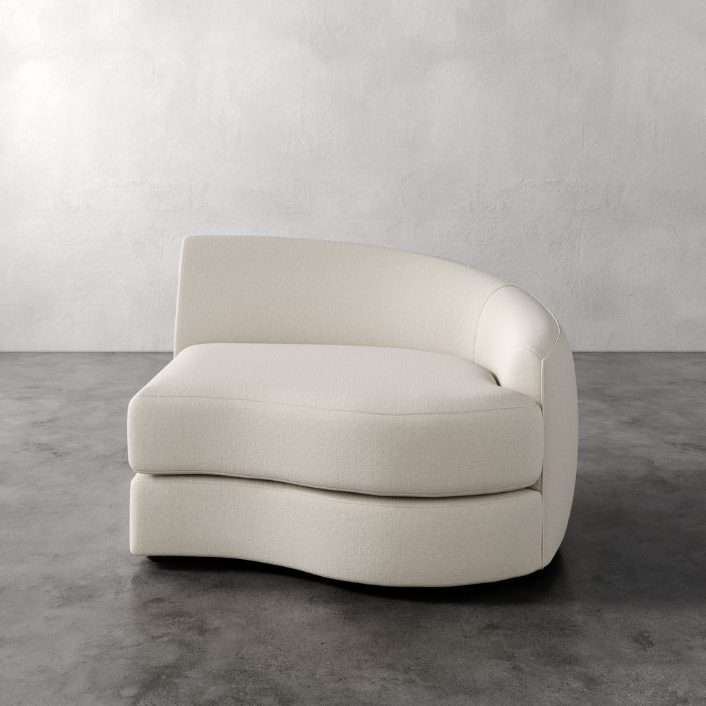 Lemieux et Cie Rulmann Right Arm Chair in ivory upholstery, curved sectional module with rounded organic form, on polished concrete floor against white textured walls.