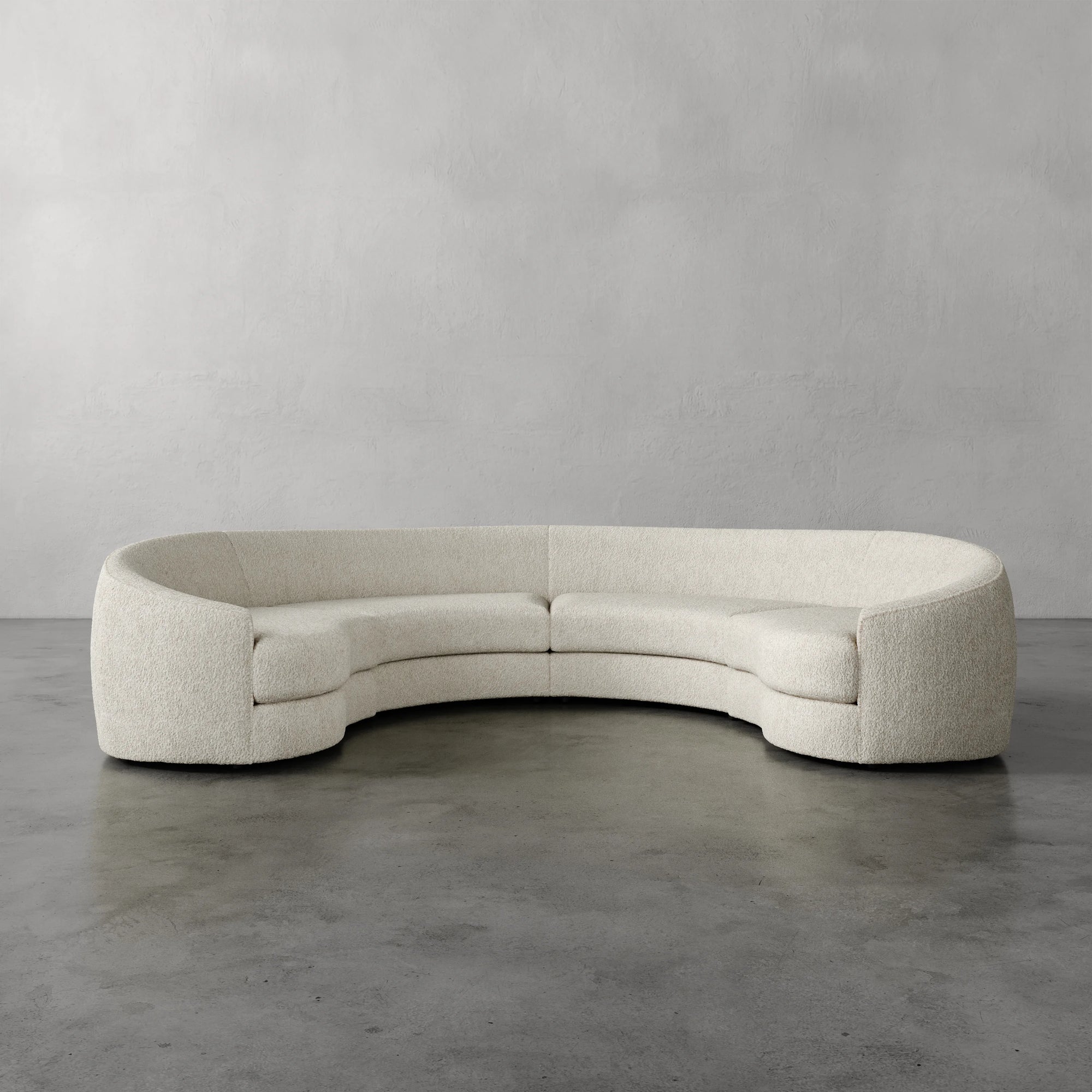 Lemieux Et Cie Rulmann 4-Piece Sectional Curved beige sofa on a gray floor with a plain gray wall background