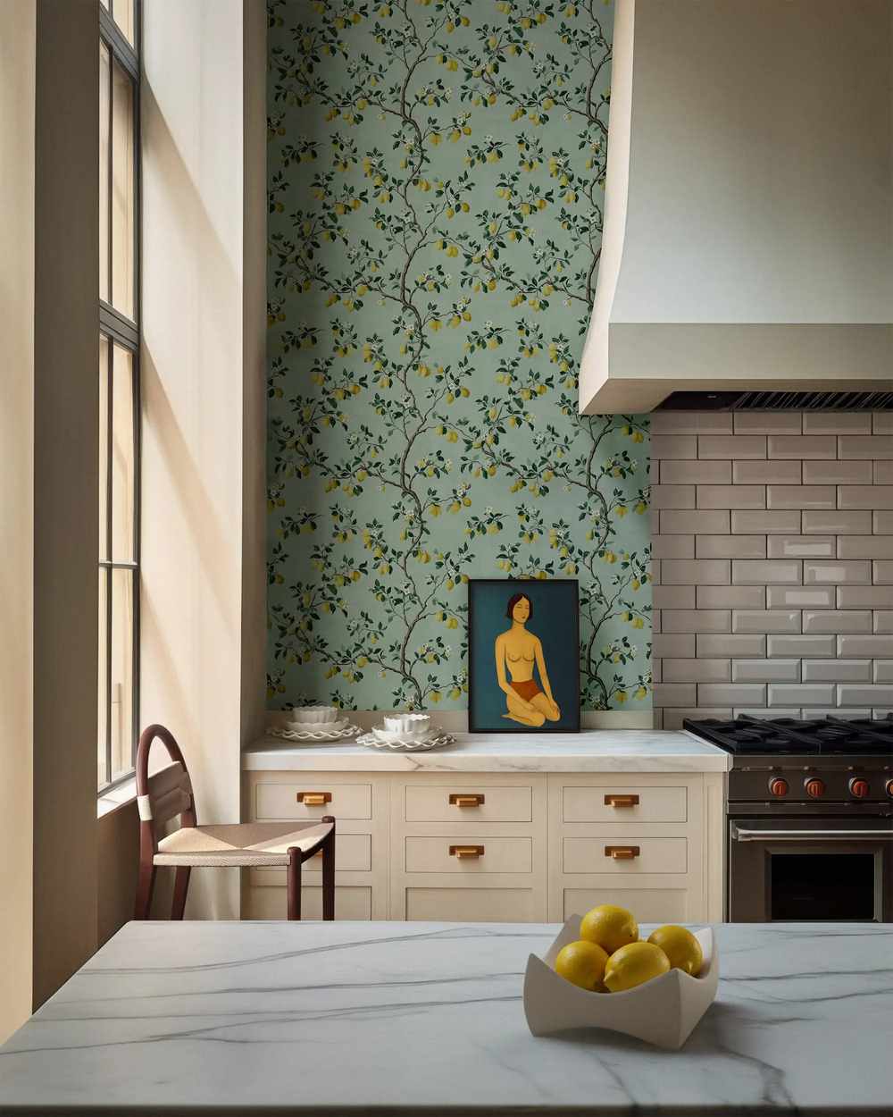 Modern kitchen styled with Lemieux et Cie Citron Verts green chinoiserie peel and stick wallpaper, featuring lemon botanicals on a mint background, paired with a marble countertop and decorative accents.