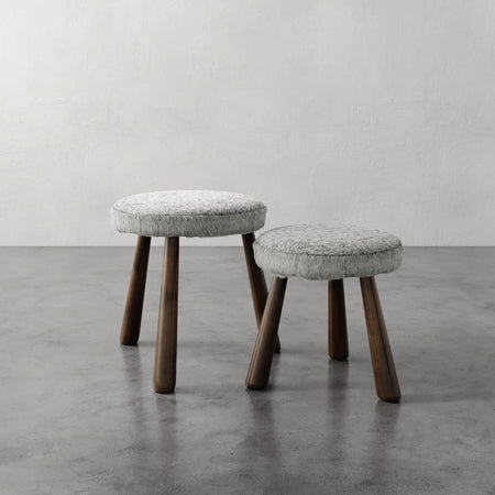 Lemieux et Cie Madeleine Leather Stool in grey with tapered legs, stackable ottomans on polished concrete floor against textured plaster walls.