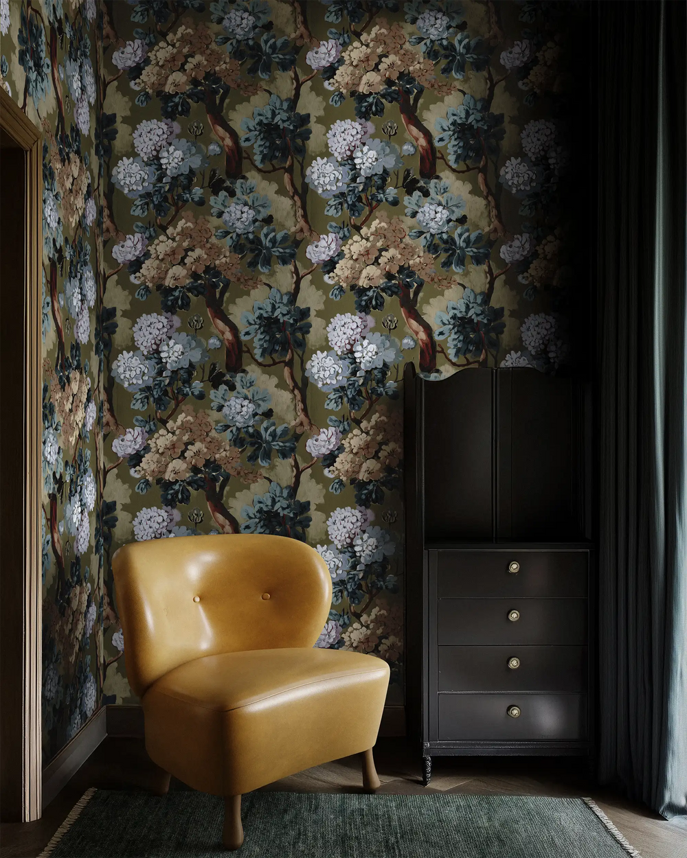 Yellow Tourenne chair and dark cabinet styled against Lemieux et Cie Folie Floral green chinoiserie peel and stick wallpaper, featuring painted blossoms on an olive background in a romantic chinoiserie design.