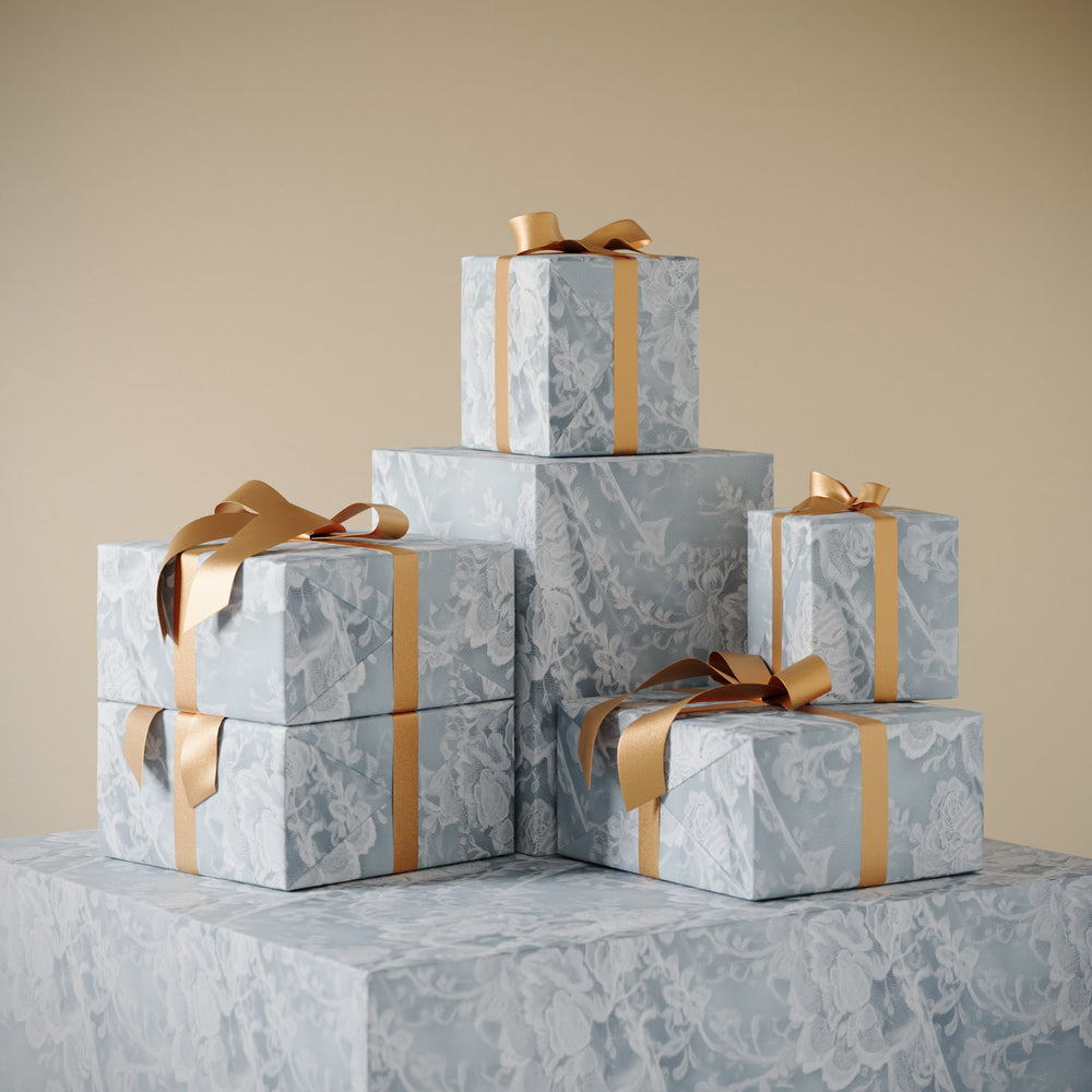 Lemieux et Cie French Lace Gift Wrapping Paper in ivory floral pattern, stacked gift boxes tied with champagne ribbon against neutral backdrop.