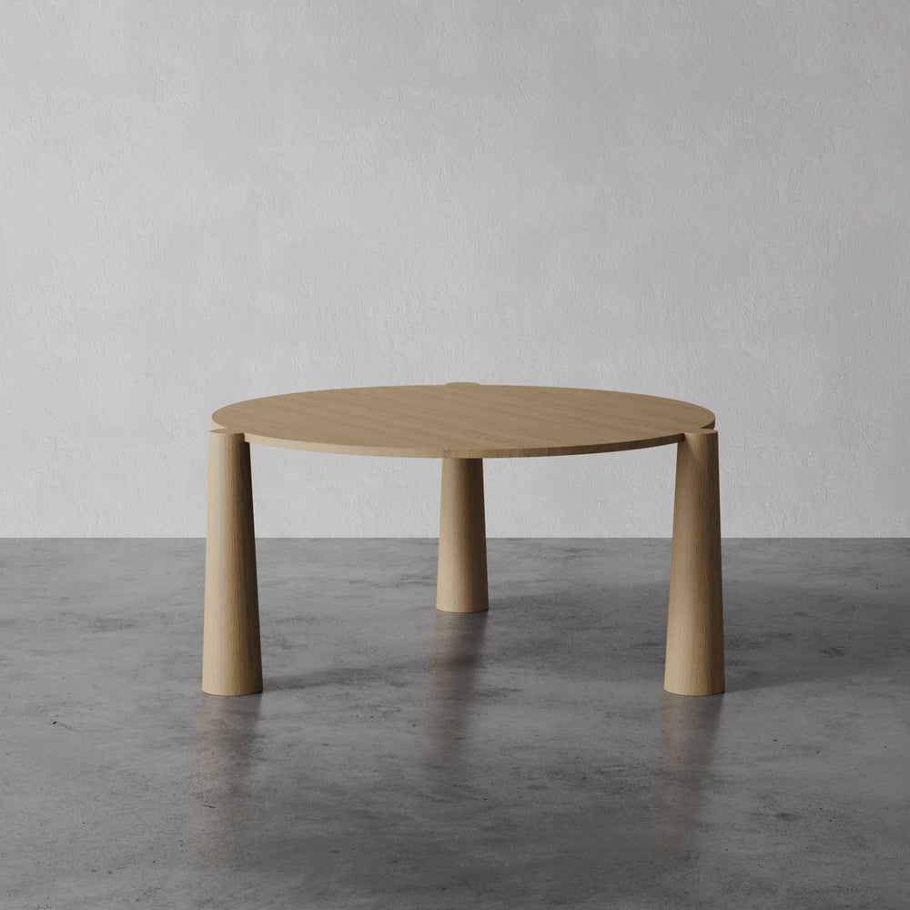 Lemieux et Cie Girard Dining Table in oak with flared cylindrical legs, shown on concrete floor against neutral studio backdrop.