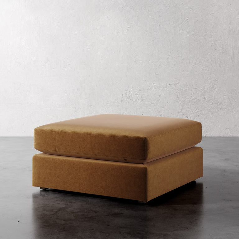 Lemieux Et Cie Chanaux Ottoman Brown ottoman on a dark floor with a white wall background