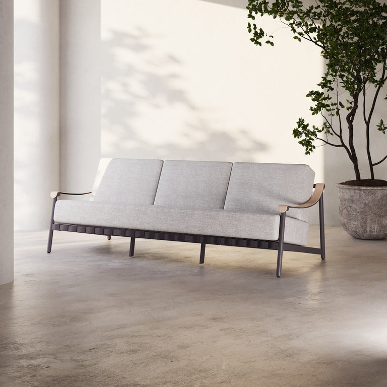 Lemieux Et Cie Hudson 3-Seat Sofa HudsonSofa An outdoor sofa with gray fabric cushions, faux all-weather leather arms, and a powder coated aluminum frame, set in a contemporary indoor-outdoor setting with a tree in the background.