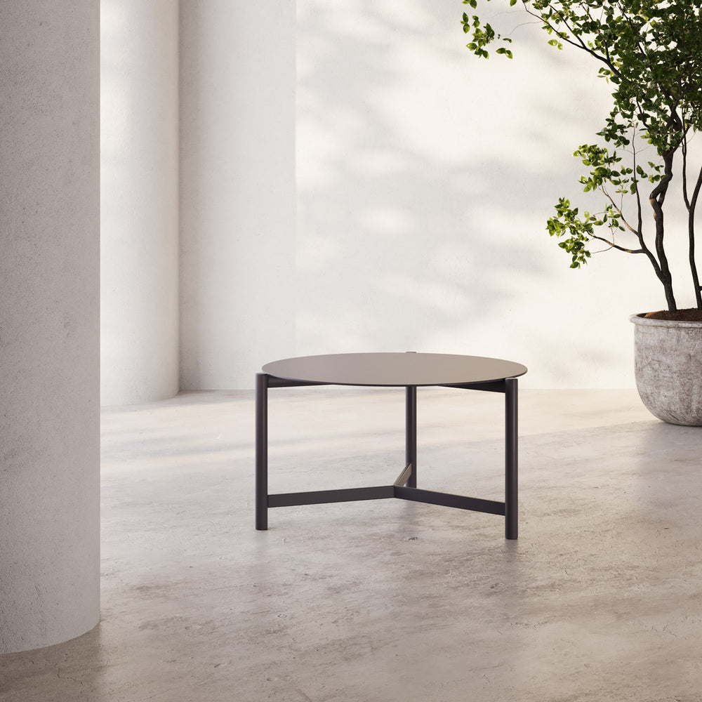 Lemieux et Cie Hudson 25" Round Side Table with dark frame and rounded top, low-profile side table on concrete floor beside potted tree.