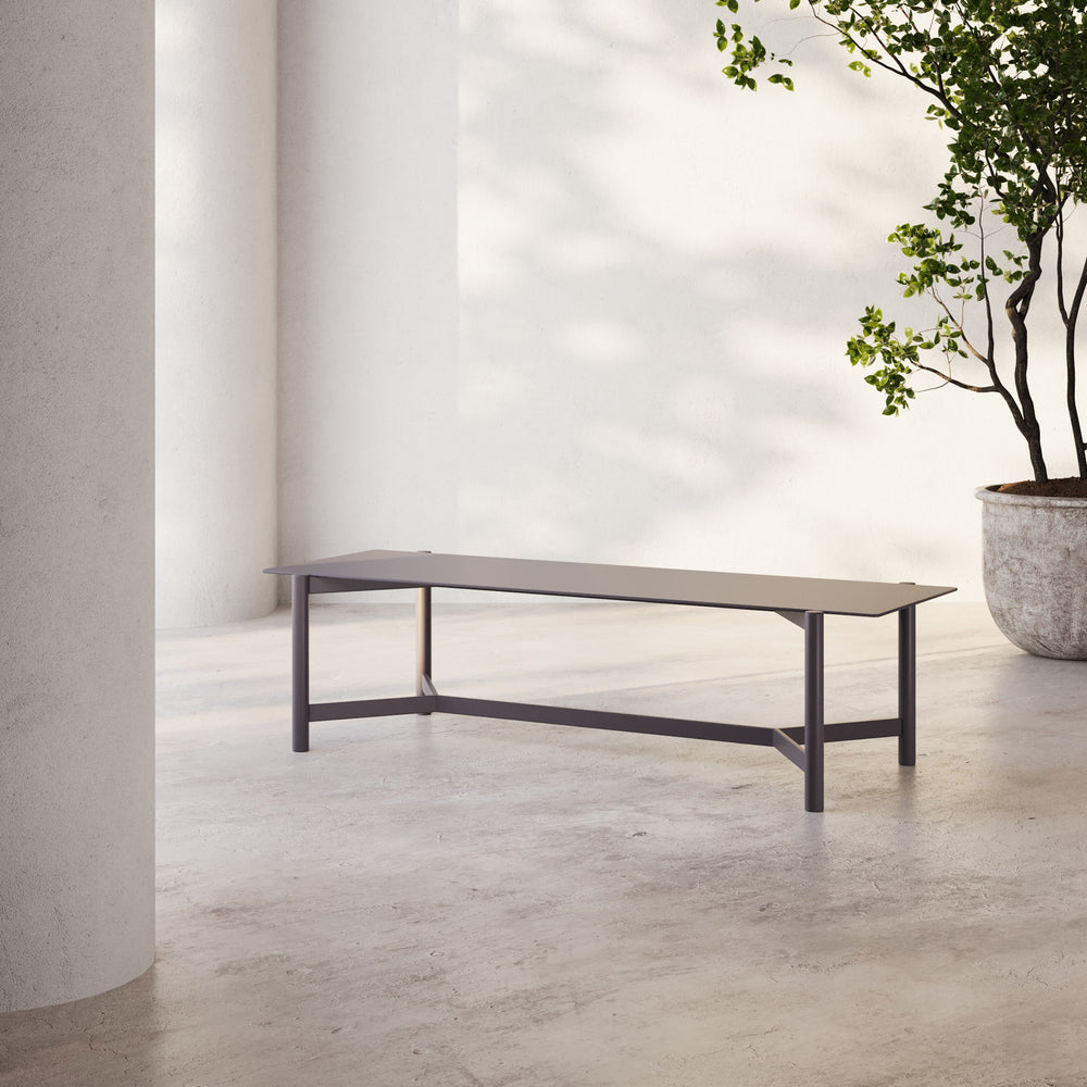 Lemieux et Cie Hudson 46" Rectangular Coffee Table with slim frame and stretcher base, shown on concrete floor in sun-dappled outdoor setting.