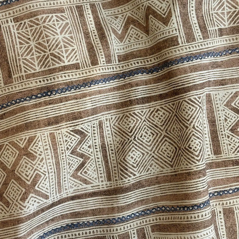 Lemieux et Cie Outdoor Pillow in Raw Umber Inlet, geometric patterned pillow with ivory, taupe and blue striped detail, close-up of draped textile.