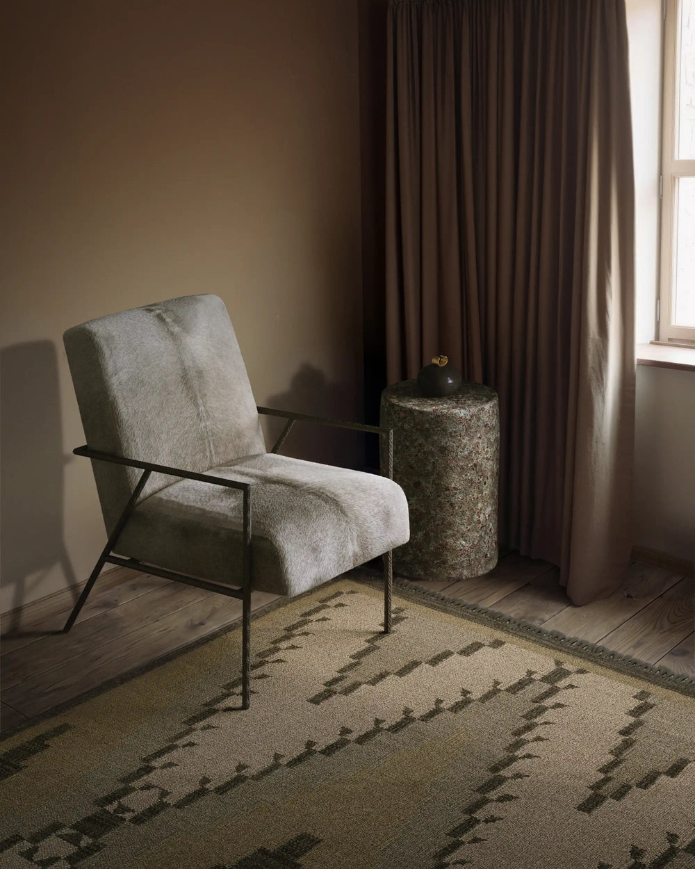 Oxidized Jade ceramic stool and end table with reactive glaze. paired with the Imane chair in hair on hide and Cluny rug in a moody soft lit room