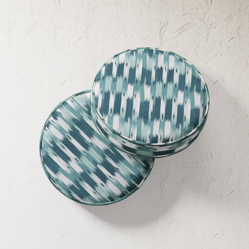 Lemieux et Cie Outdoor Pillow in Teal French Flamme ikat pattern, round cushions stacked on textured plaster wall in soft daylight.