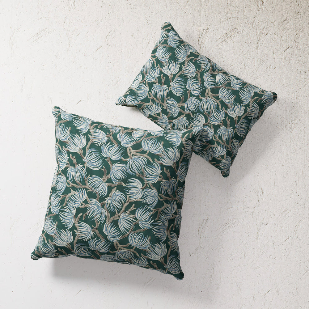 Lemieux et Cie Winding Palm Plant Outdoor Pillow in teal with botanical motif, two pillows shown on textured plaster backdrop.