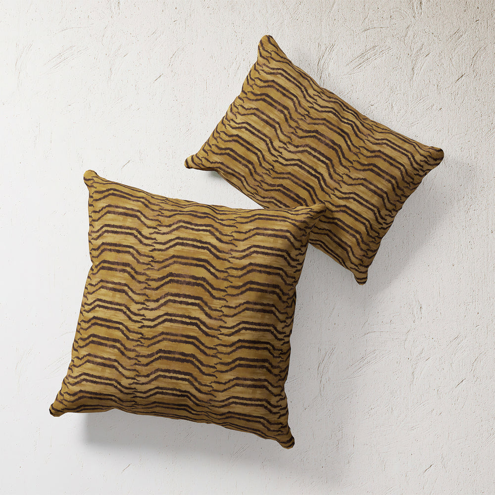 Lemieux et Cie Tiger Stripe Outdoor Pillow in golden ochre and brown, decorative pillows shown against textured white plaster wall.