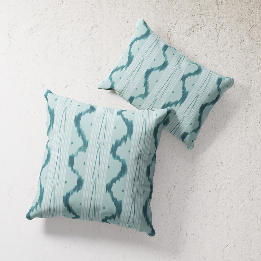 Lemieux et Cie Outdoor Pillow in teal ikat wave pattern, square throw pillows with geometric stripes and organic motifs, shown on textured plaster wall.