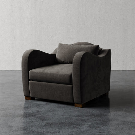 Lemieux et Cie Elodie Chair, charcoal upholstered lounge chair on wood legs, shown on polished concrete floor against textured plaster wall.