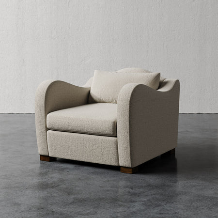 Lemieux et Cie Elodie Chair, textured upholstered lounge chair with curved arms and wood legs, shown on polished concrete floor against neutral plaster walls.