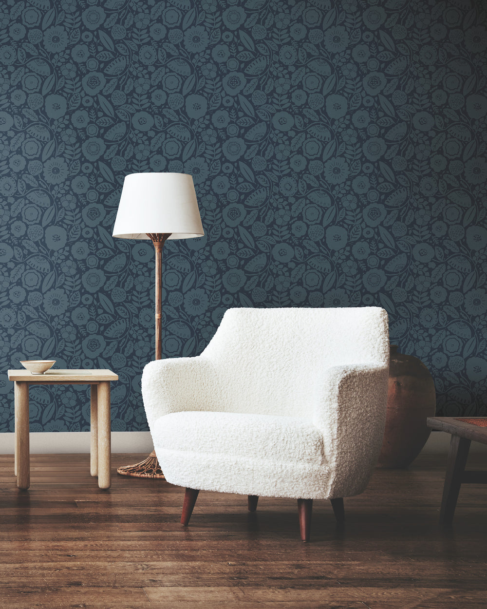 Lemieux et Cie Camelia Blossom wallpaper in cobalt and indigo blue with floral motif, shown behind ivory bouclé chair and table lamp on wood floors.