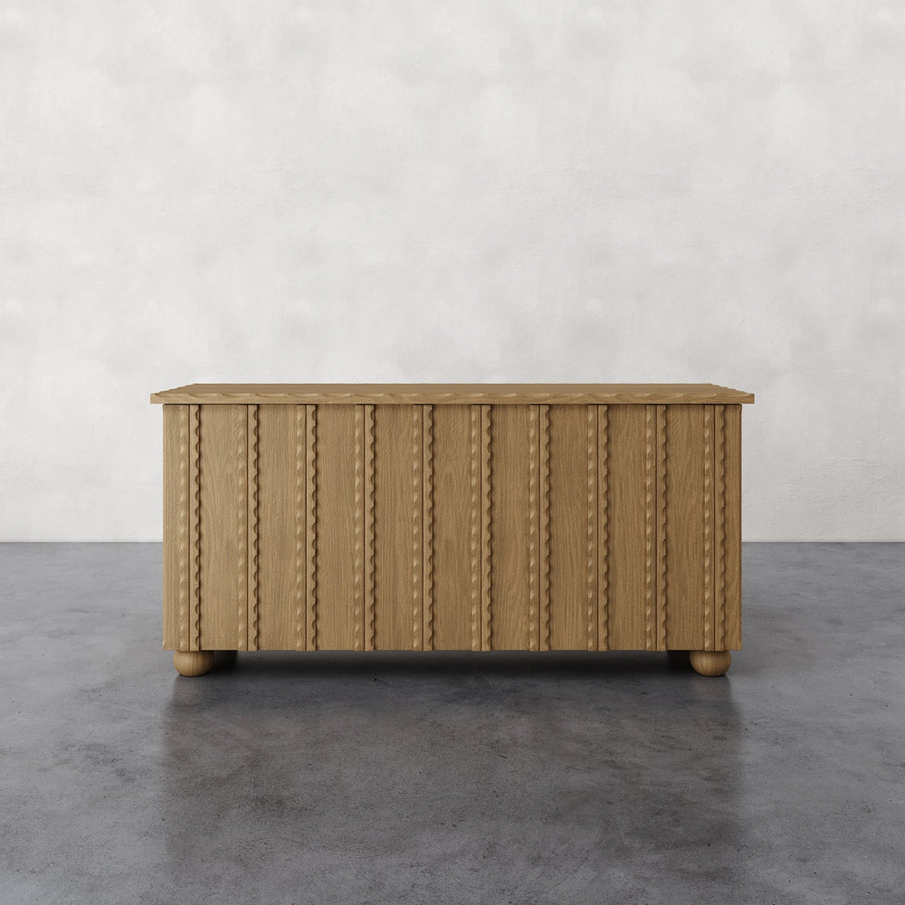 Lemieux et Cie Marchand 4-Door Cabinet with vertical reeded detailing and turned feet, low console shown on concrete floor against white wall.