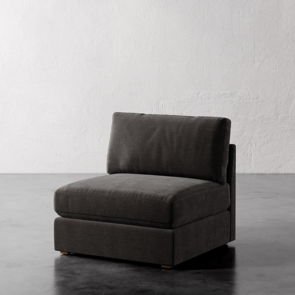 Lemieux et Cie Chanaux Armless Chair in charcoal upholstery, modular seating piece on dark concrete floor against textured white plaster wall.