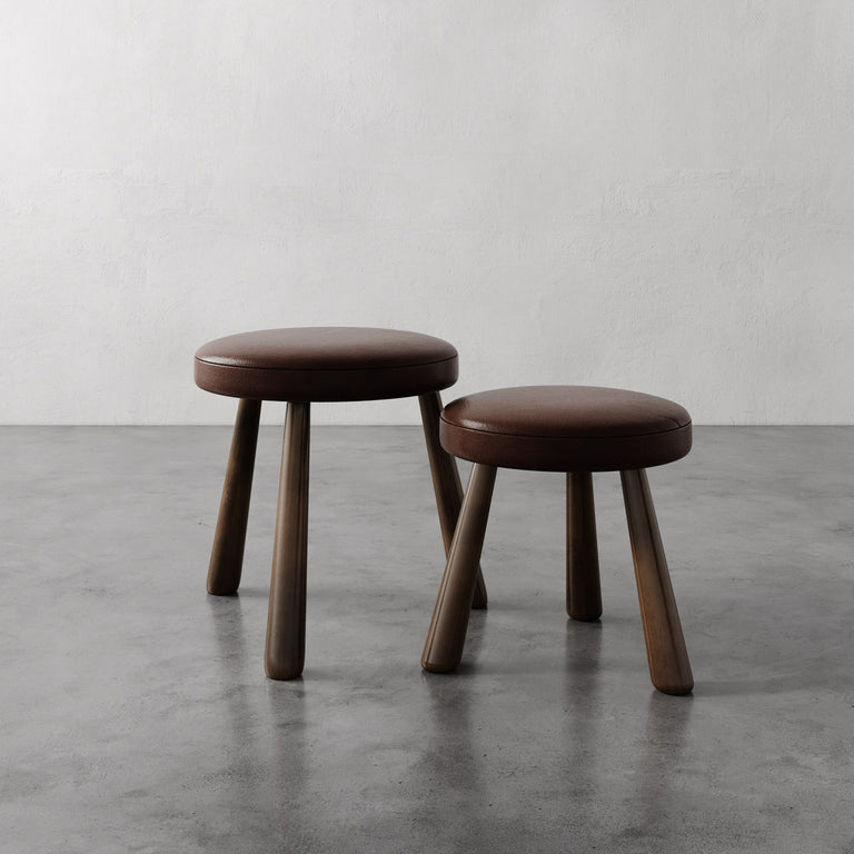 Lemieux et Cie Madeleine Leather Stool in tobacco, hand-upholstered stools with tapered legs, shown on polished concrete floor against white plaster wall.