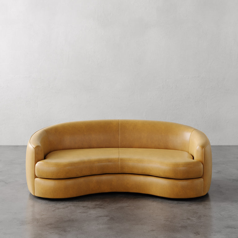 Lemieux et Cie Yellow curved Rulmann leather sofa on a gray floor with a light gray wall background