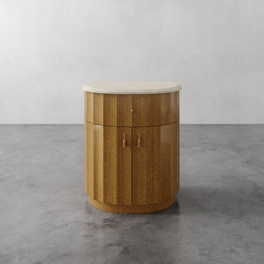 Lemieux et Cie Ondara Fluted Nightstand in champagne eucalyptus with honed travertine top, nightstand with brass tassel hardware on concrete floor.
