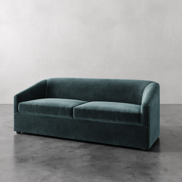 Lemieux et Cie Arvelle Queen Sleeper in deep teal, curved-arm sofa shown on polished concrete floor against neutral plaster wall.