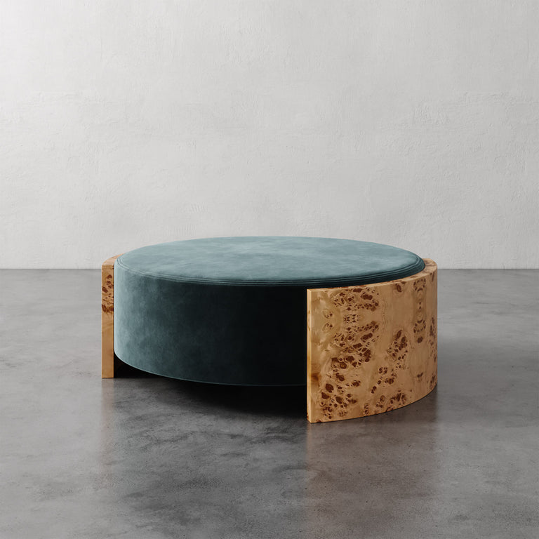 Lemieux et Cie Benoit Coffee Table Ottoman in teal velvet and wire-brushed oak, circular low-profile ottoman on concrete floor against neutral plaster walls.