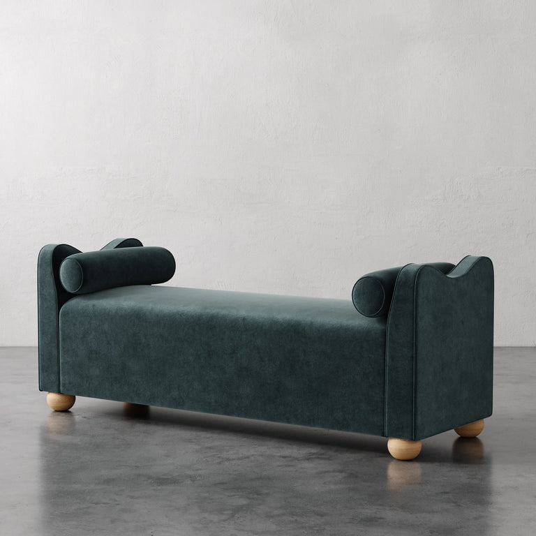 Lemieux et Cie Danielle Upholstered Bench in deep teal with sculptural cylindrical bolsters and rounded legs, shown on polished concrete floor against white plaster walls.