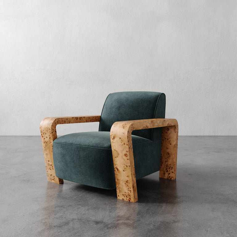 Lemieux et Cie Dumas Chair in deep teal upholstery with burled arms and legs, lounge chair shown on polished concrete floor against white plaster walls.