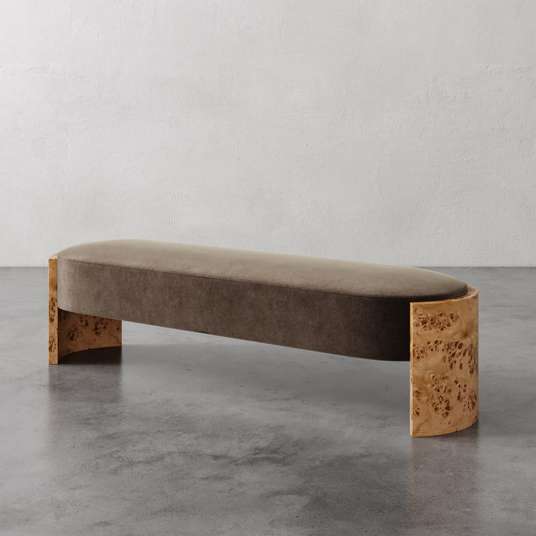Lemieux et Cie Benoit Custom Upholstered Bench with curved maple burl legs and taupe upholstered seat, shown on concrete floor against plaster wall.