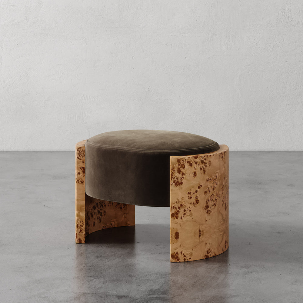 Lemieux et Cie Benoit Ottoman in oak burl and olive velvet, curved slab ottoman with sculptural low profile, shown on polished concrete floor against white plaster wall.