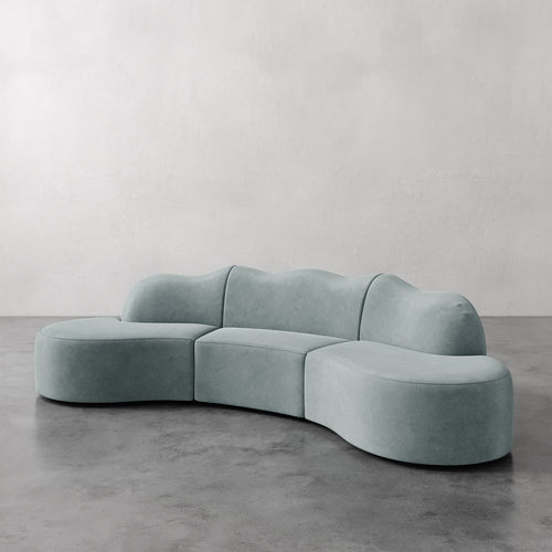 Lemieux et Cie Serpentine Sectional Sofa in sage upholstery, modular curved form on polished concrete floor against white plaster wall