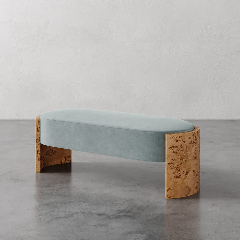 Lemieux et Cie Benoit Custom Upholstered Bench in pale blue with curved Maple burl legs, low-profile seating shown on polished concrete floor against textured plaster walls.