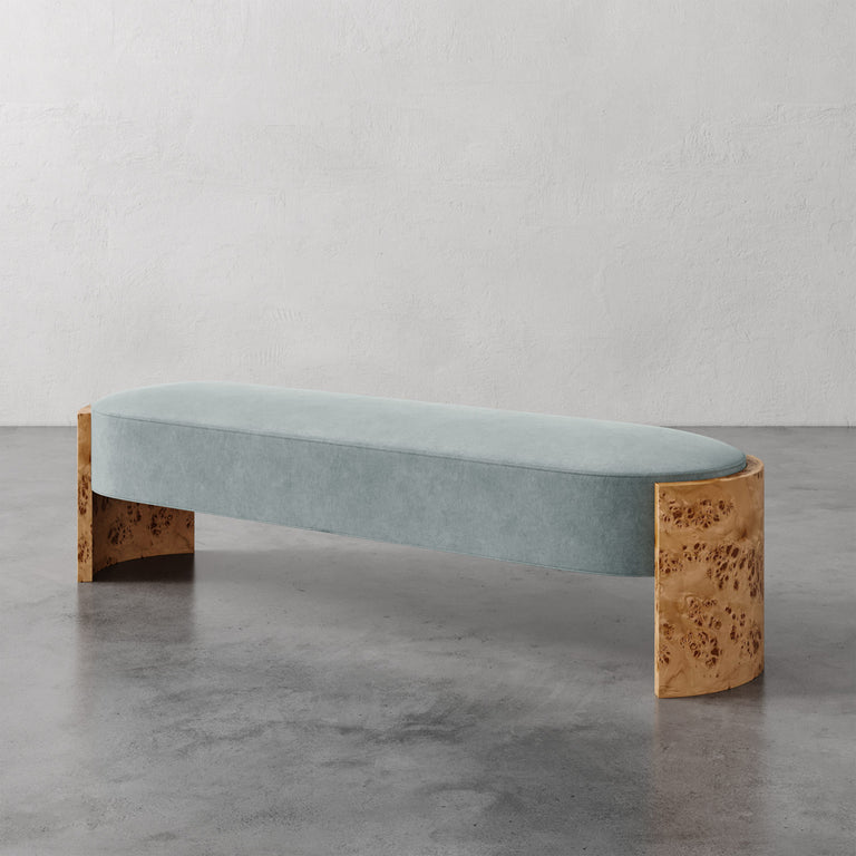 Lemieux et Cie Benoit Custom Upholstered Bench with curved maple burl legs and pale blue upholstered seat, shown on polished concrete floor against neutral plaster wall.