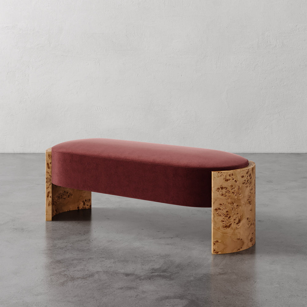 Lemieux et Cie Benoit Custom Upholstered Bench in rust velvet with curved Maple burl legs, shown on polished concrete floor against textured plaster wall.