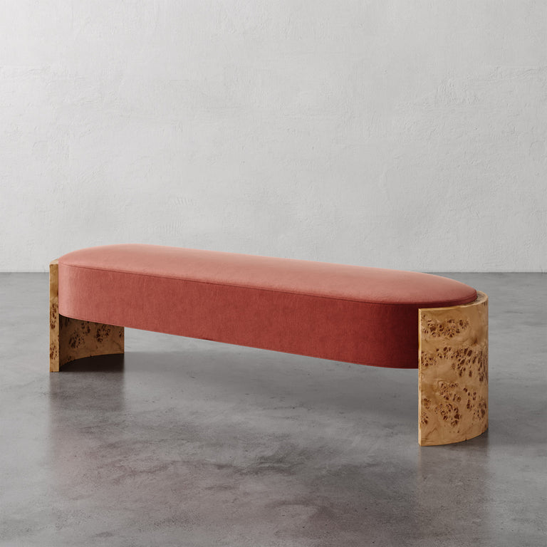 Lemieux et Cie Benoit Custom Upholstered Bench in coral velvet with curved Maple burl legs, shown on polished concrete floor against textured plaster wall.