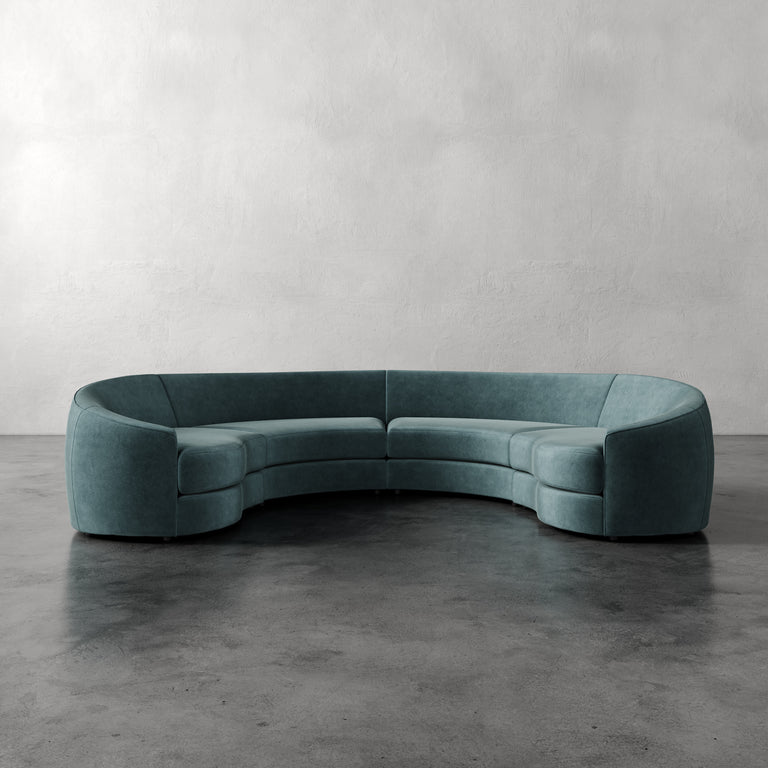 Lemieux et Cie Rulmann 4-Piece Sectional in sage green, curved modular sofa on dark concrete floor against textured plaster walls.