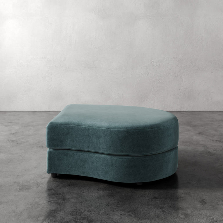 Lemieux Et Cie Rulmann Right Ottoman Teal ottoman on a gray floor with a plain white wall background