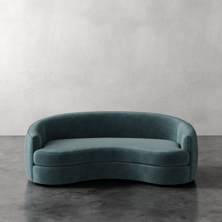 Lemieux et Cie Rulmann Sofa in deep teal, curved sculptural sofa with organic rounded form, set against textured plaster walls on dark polished concrete floor.
