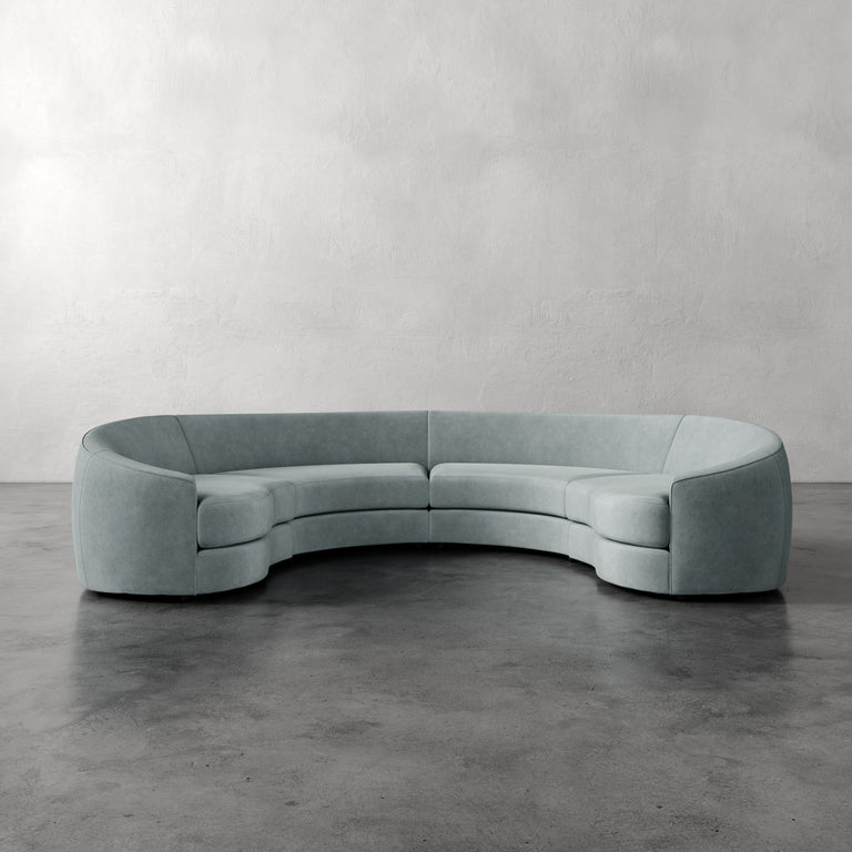 Lemieux et Cie Rulmann 4-Piece Sectional in soft sage green, curved modular sofa on polished concrete floor against textured plaster wall.