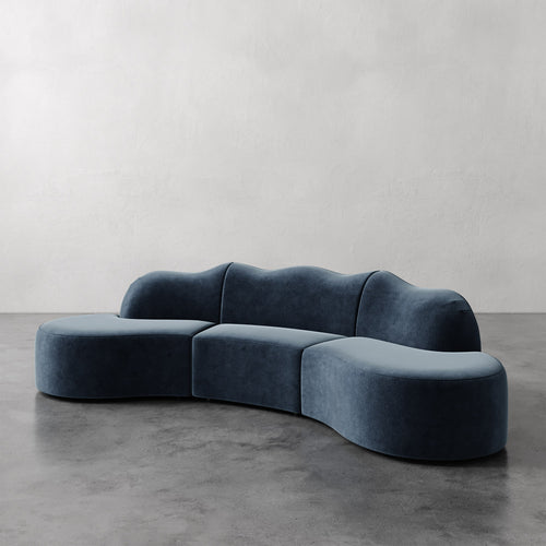 Lemieux et Cie Serpentine Sectional Sofa in blue-gray upholstery, organic curved form with rounded edges, shown on polished concrete floor against neutral walls.