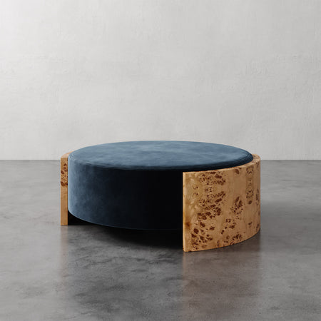 Lemieux et Cie Benoit Coffee Table Ottoman with wire-brushed oak burl panel and deep blue upholstered cushion, shown on polished concrete floor.