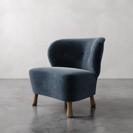 Lemieux et Cie slipper chair in slate blue upholstery with sculptural rounded legs, shown on polished concrete floor against neutral walls.