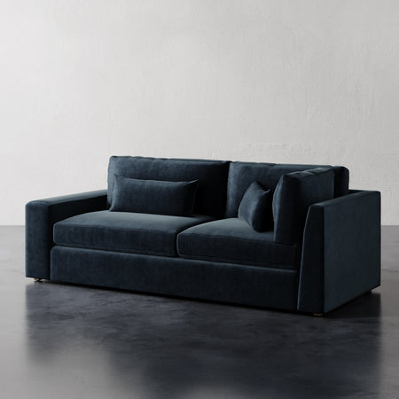 Lemieux et Cie Lacroix sofa in deep teal velvet upholstery, two-seat sofa with square arms and bolster pillows, on dark wood floors against white plaster walls.