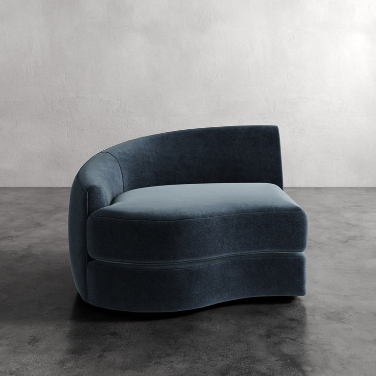 Lemieux Et Cie Rulmann Left Arm Chair Blue curved sofa in a minimalistic room with gray walls and floor.