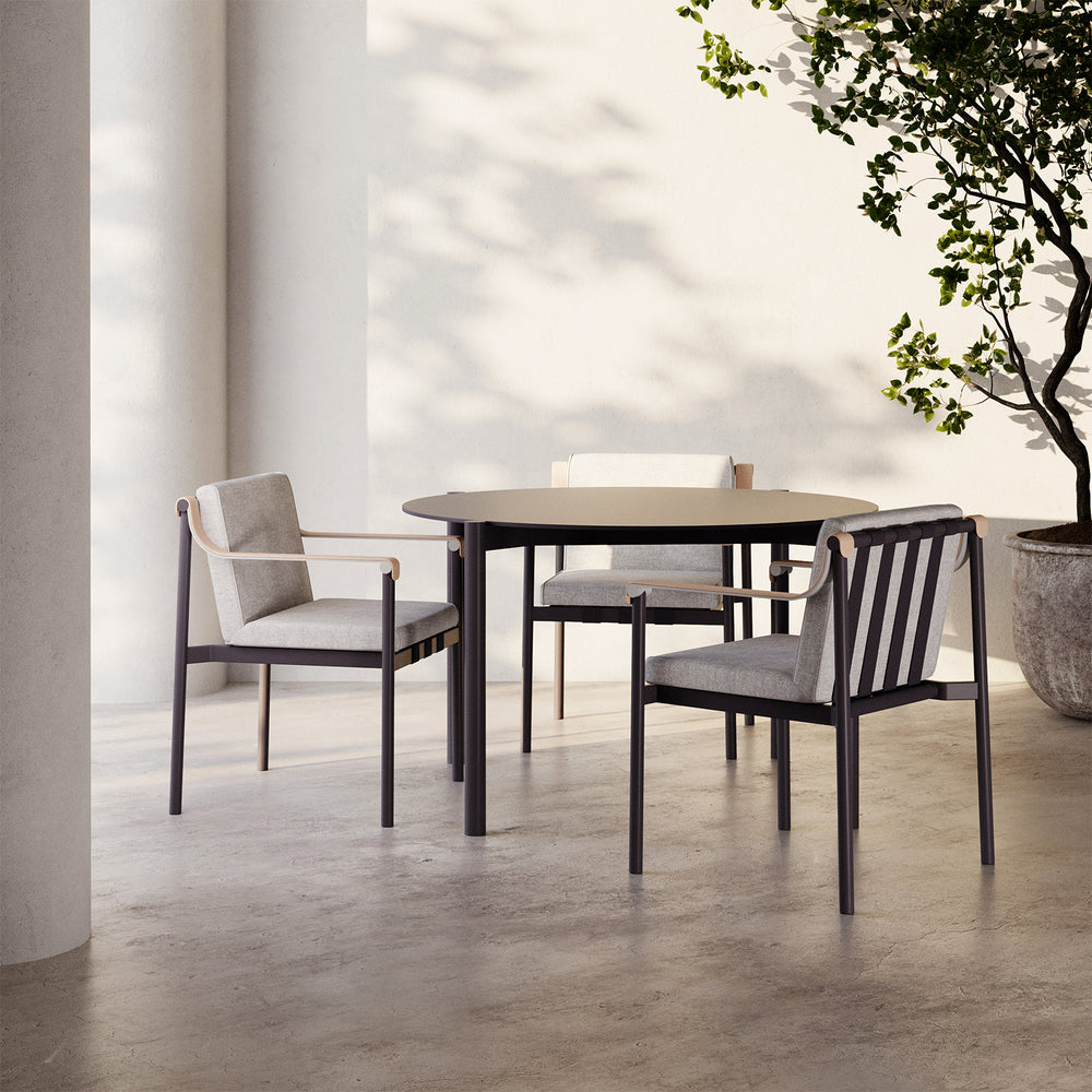 Lemieux et Cie Hudson 47" Round Dining Table with dark slim legs and neutral round top, dining table shown on concrete floors in sunlit outdoor patio with white walls and greenery