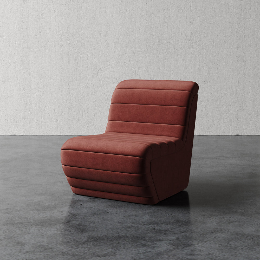 Lemieux et Cie Brunoy Chair, channel-tufted slipper chair in terracotta upholstery, sculptural low-profile silhouette on polished concrete floor against textured plaster walls.