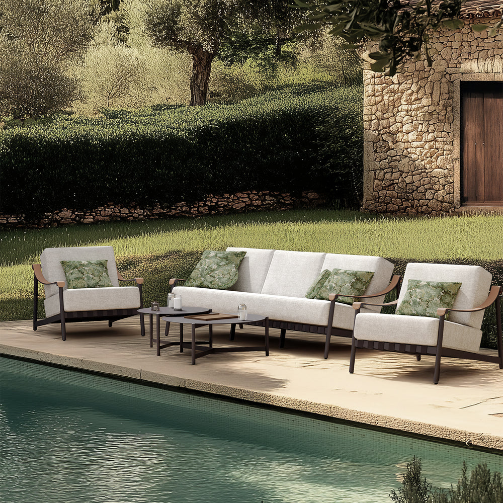 Lemieux et Cie Hudson Round Side Table, slim low-profile form on outdoor terrace beside pool with stone wall and lawn.
