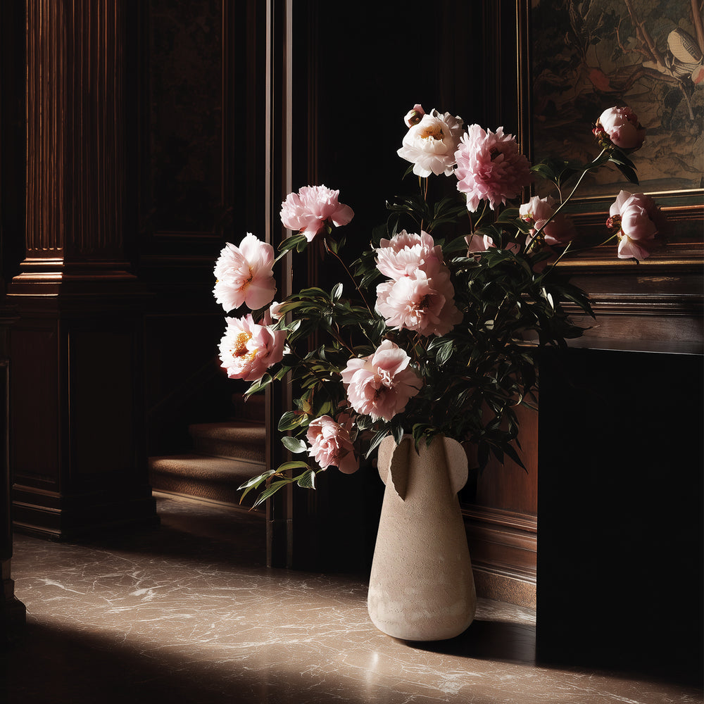 Lemieux et Cie Anouar Vase Collection in buff, tapered pitcher-form vase with blush peonies, dark wood-paneled walls and marble flooring in warm light.