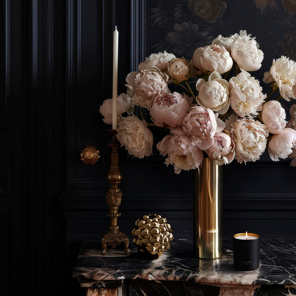 Lemieux et Cie Tubéreuse de Kalimantan Filled Candle in dark vessel on marble surface, styled with brass candlestick and peonies against dark paneled walls.